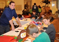 Kulturvermittler Erich Stadlbauer steht lächelnd vor Tischen, an denen Kinder mit Papier und Stiften basteln.