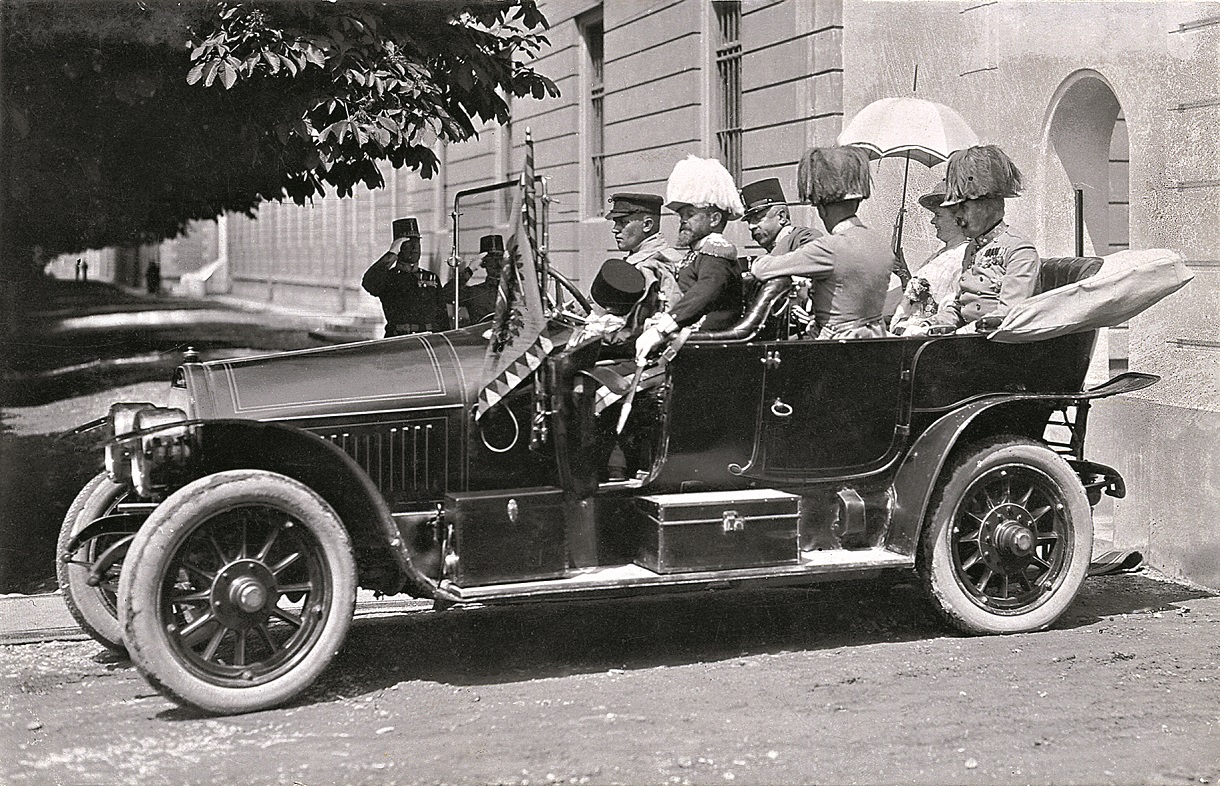 Schwarz-Weiß-Foto mit sechs Personen in einem Auto mit offenem Verdeck.