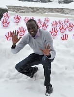 Vor dem Transparent im Schnee kniender und lächelnder Mann mit erhobenen Händen