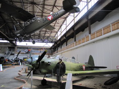 Schaufensterpuppe in Pilotenuniform neben einem Militärflugzeug im Hangar.