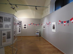 Ausstellungsraum mit Schautafeln mit Fotos und Infotexten, dazwischen Wimpel.