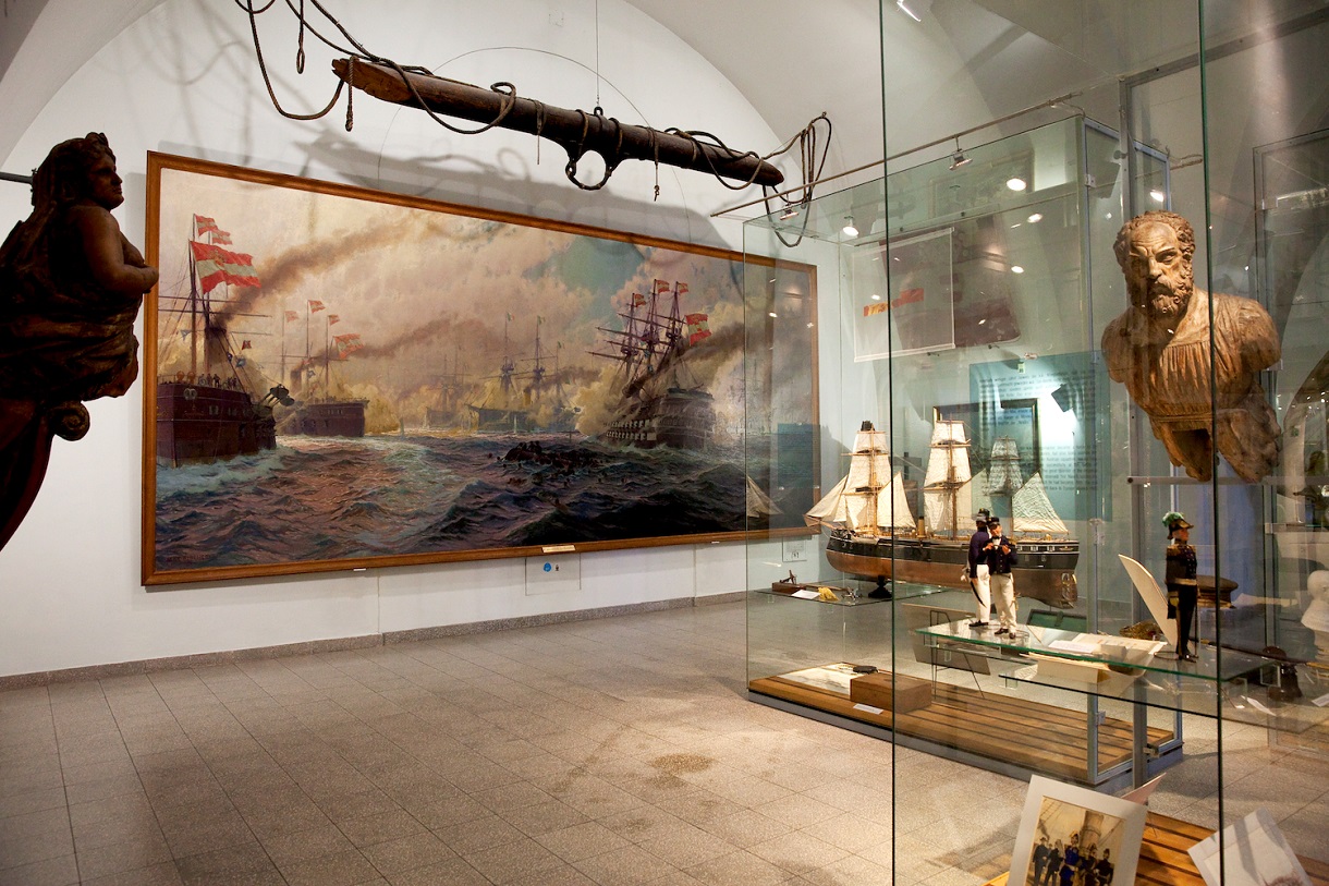 Galionsfiguren links und rechts, in der Mitte ein großes Gemälde mit Kriegsschiffen, daneben ein Segelschiffmodell