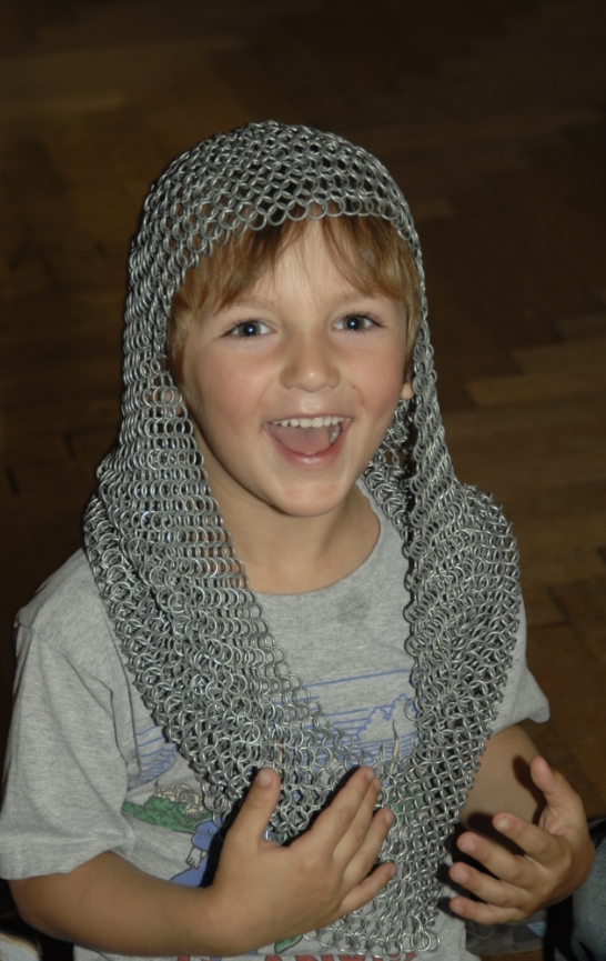 Lachendes Kind mit einem Kettenhemd über Kopf und Schultern.