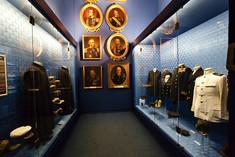 Schmaler Raum mit Schaukästen voller Uniformen links und rechts, geradeaus schön gerahmte Porträts verschiedener Marinegeneräle.
