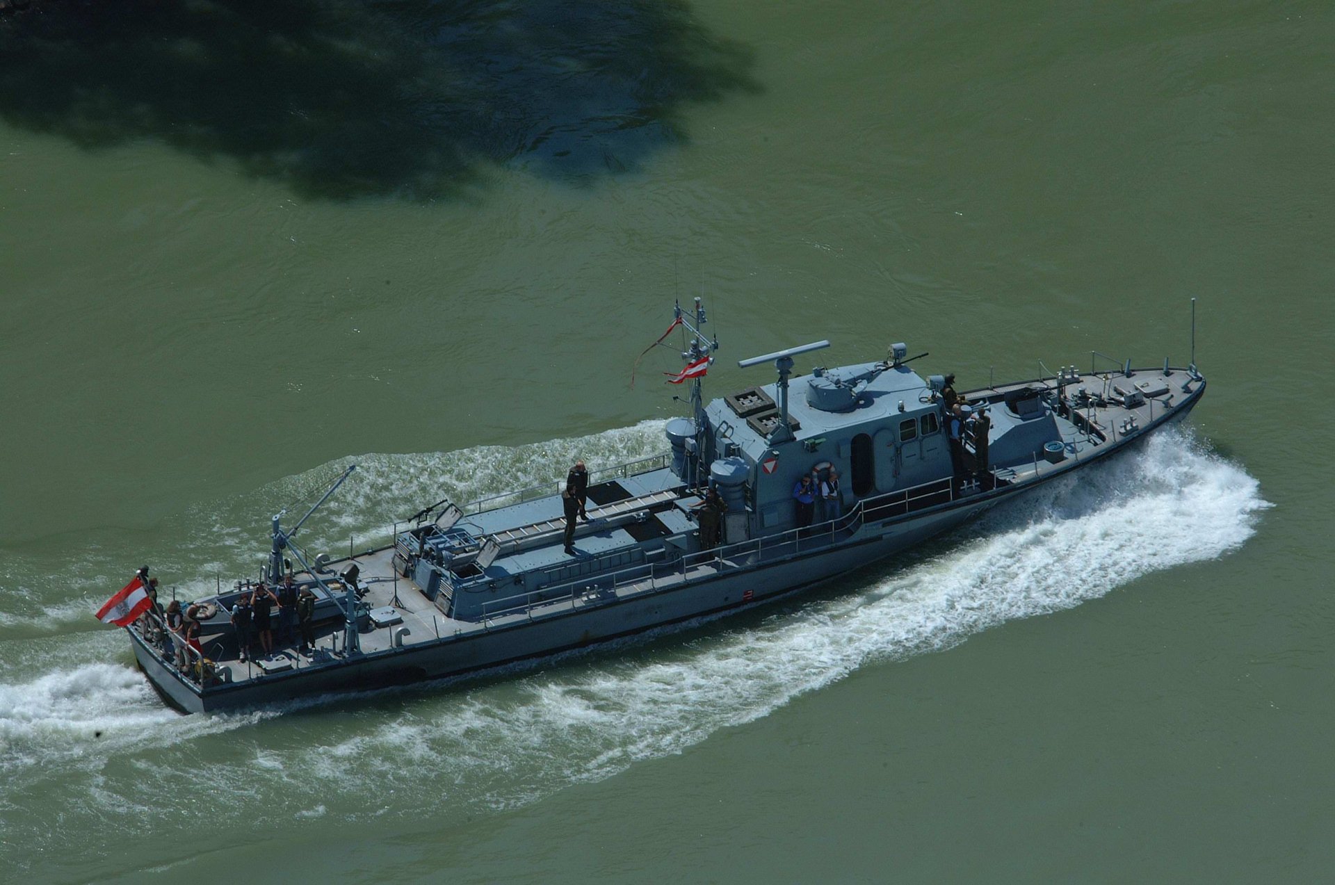 Dieses Bild zeigt das Patrouillenboot "Niederösterreich" im Wasser, fotografiert von der Vogelperspektive. Mitfahrende Gäste und Mitarbeitende stehen verteilt auf dem Boot.