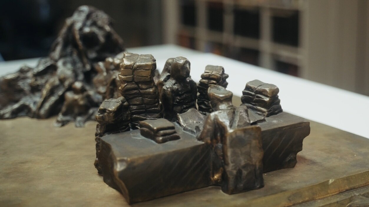 Bronzene Figuren sitzen hinter massiven Schreibtischen, umgeben von Aktenbergen – die Skulptur ,,Der Schreibtischtäter"