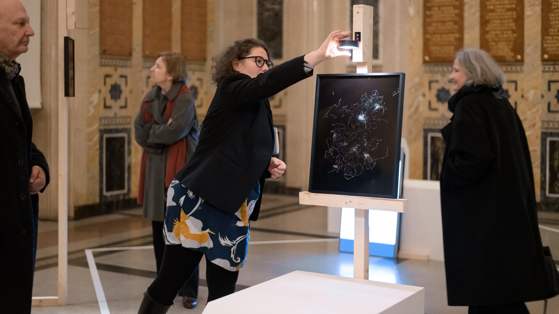 Auf diesem Bild sieht man die Künstlerin Raffaela Bielesch vor einem Bild mit schwarzen Hintergrund, dekoriert mit Düppel-Streifen. 