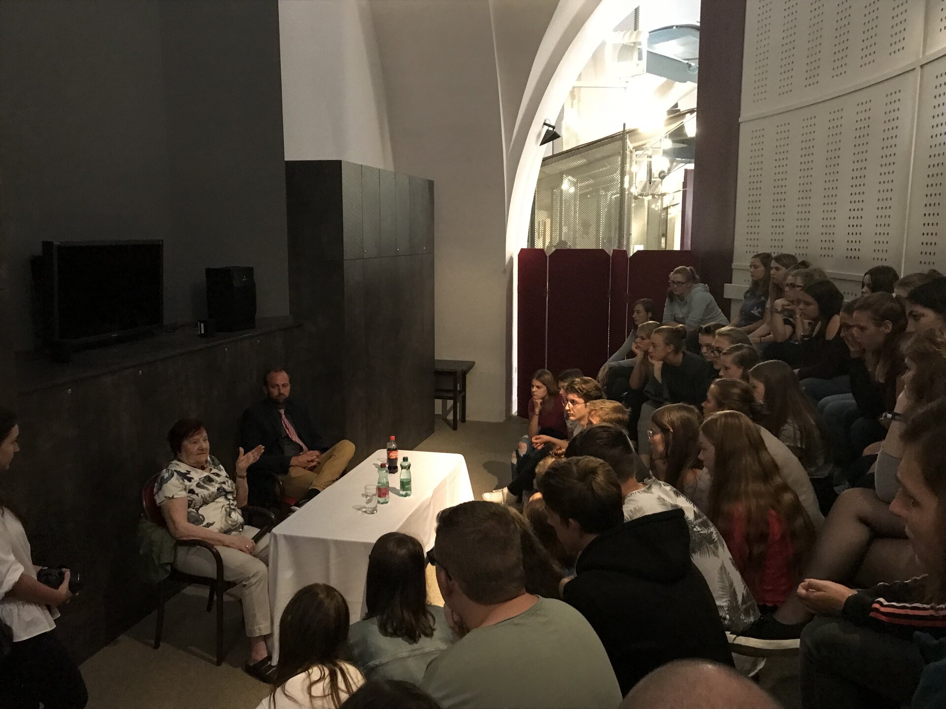  Das Bild zeigt eine Gruppe Jugendlicher, die vor Anna Lehr Splawinski sitzen. Anna Lehr Splawinski spricht über ihre Tätigkeit als Meldegängerin des polnischen Widerstands beim Warschauer Aufstand 1944. Neben ihr sitzt der Kulturvermittler Herr Mag. Georg Rütgen, der die Veranstaltung begleitet. Die Jugendlichen hören aufmerksam zu, während Anna ihre eindrucksvollen Erfahrungen teilt.