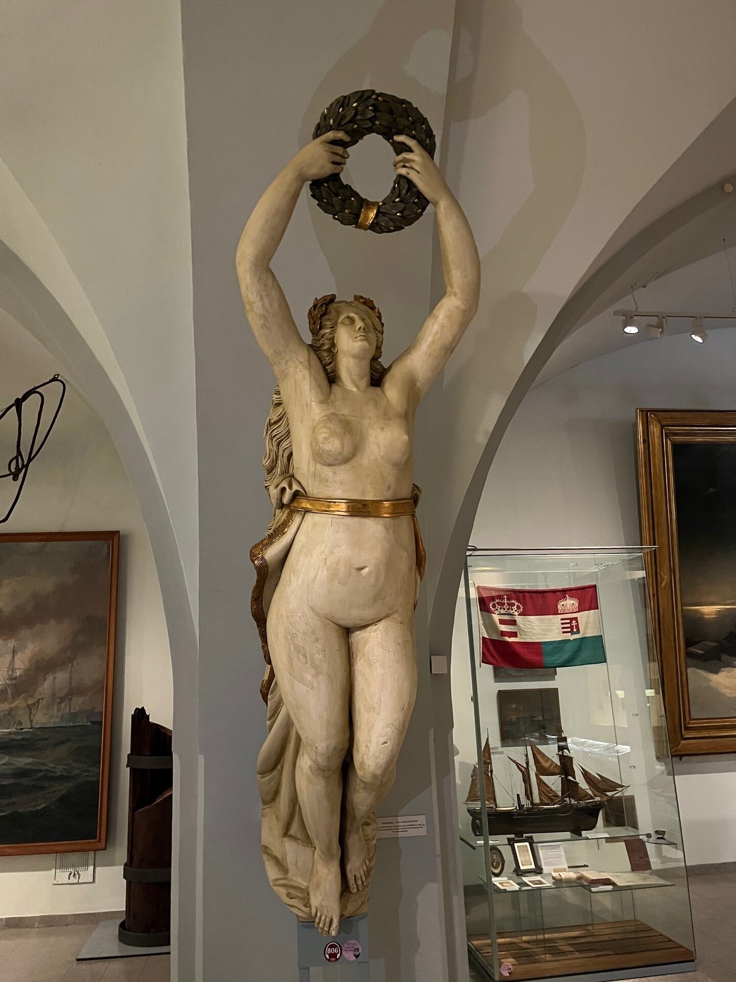 Das Bild zeigt die nackte Galionsfigur der Korvette Helgoland, dargestellt als weibliche „Meer Fee“ mit fließenden Haaren, die anmutig und elegant gestaltet ist und den Bug des Kriegsschiffs schmückte.   