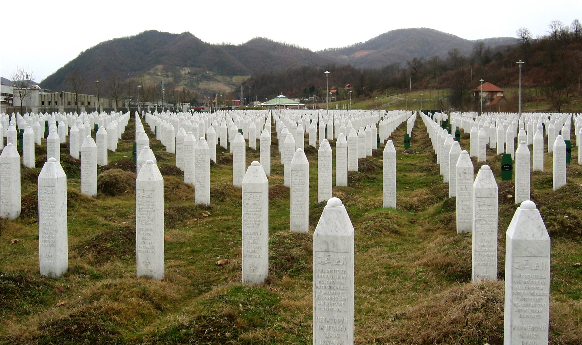 Auf diesem Bild sieht man eine Gedenk-Grabstätte mit weißen Grabsteinen auf grüner Wiese. 