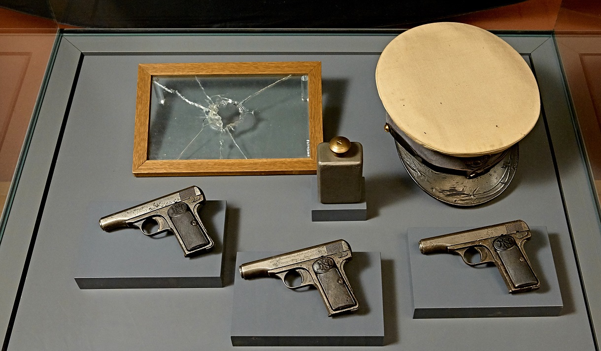 © © Peter Svec (peter.svec@pixXL.at) Das Bild zeigt eine Vitrine mit den Waffen, mit denen die Attentäter von Sarajevo auf ihren Moment warteten: Pistolen vom Typ Browning M.1910/12 und eine Handgranate vom System Kragujevacjene. Neben diesen Waffen liegt ein Hut, der von einem der Attentäter getragen wurde. Auf der anderen Seite der Vitrine befindet sich eine Scheibe mit einem Einschussloch, ein Überbleibsel des Attentats.