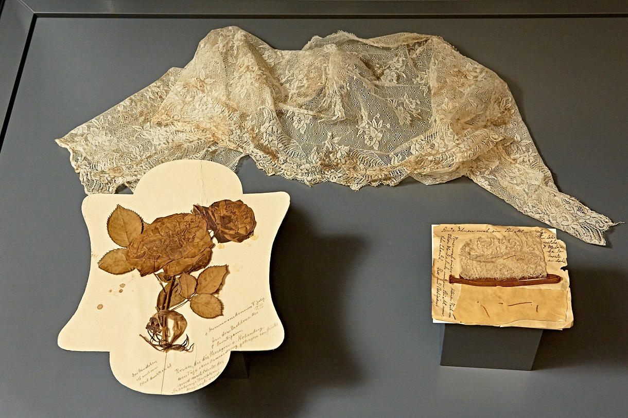 © © Peter Svec (peter.svec@pixXL.at) Das Bild zeigt eine Spitzenjacke, die die Herzogin Sophie Chotek bis zum letzten Moment trug, zusammen mit getrockneten Rosen und Briefen, die in einer Vitrine ausgestellt sind. Sie ermöglichen den Besuchern, eine Verbindung zu Sophies Leben und ihrem Schicksal herzustellen und reflektieren die menschlichen Tragödien hinter den politischen Umwälzungen jener Zeit.