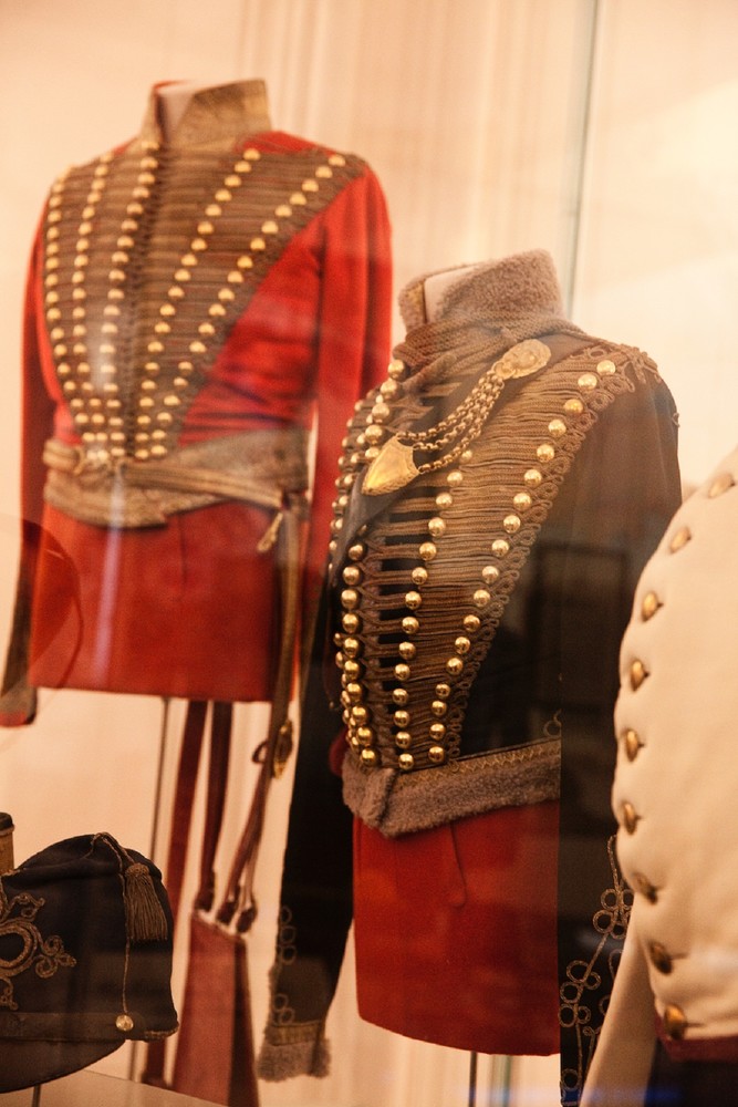 Das Bild präsentiert zwei historisch prächtige Militäruniformen mit goldenen Verzierungen, die in einer Vitrine ausgestellt sind. 